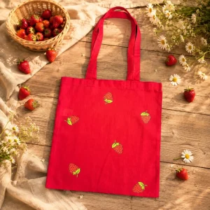 Tote bag fraise rouge en coton posé sur une table en bois avec des fraises fraîches